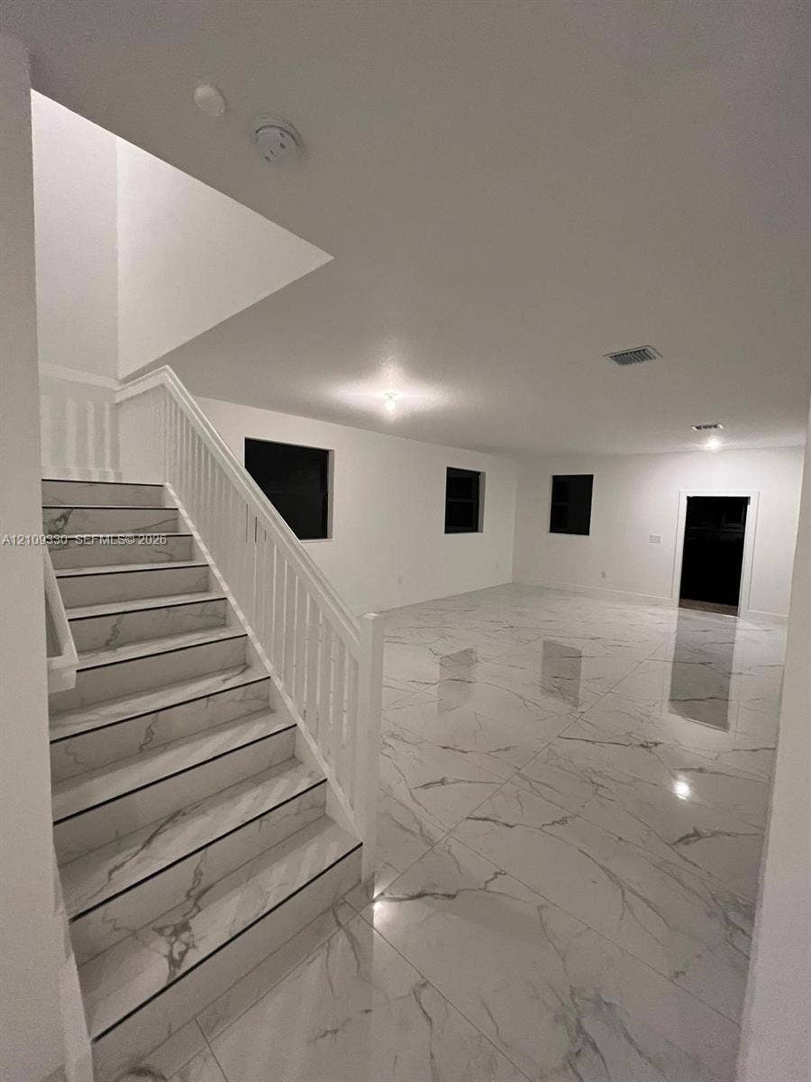 Large-format stone-finish flooring with veining detail and staircase featuring matching stone-finish treads, white balustrades, and handrail