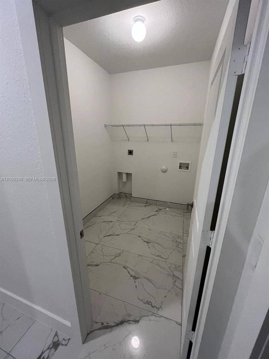 Utility space featuring large-format tile flooring with a neutral veining pattern, built-in wire shelving, and dedicated washer and dryer hookups