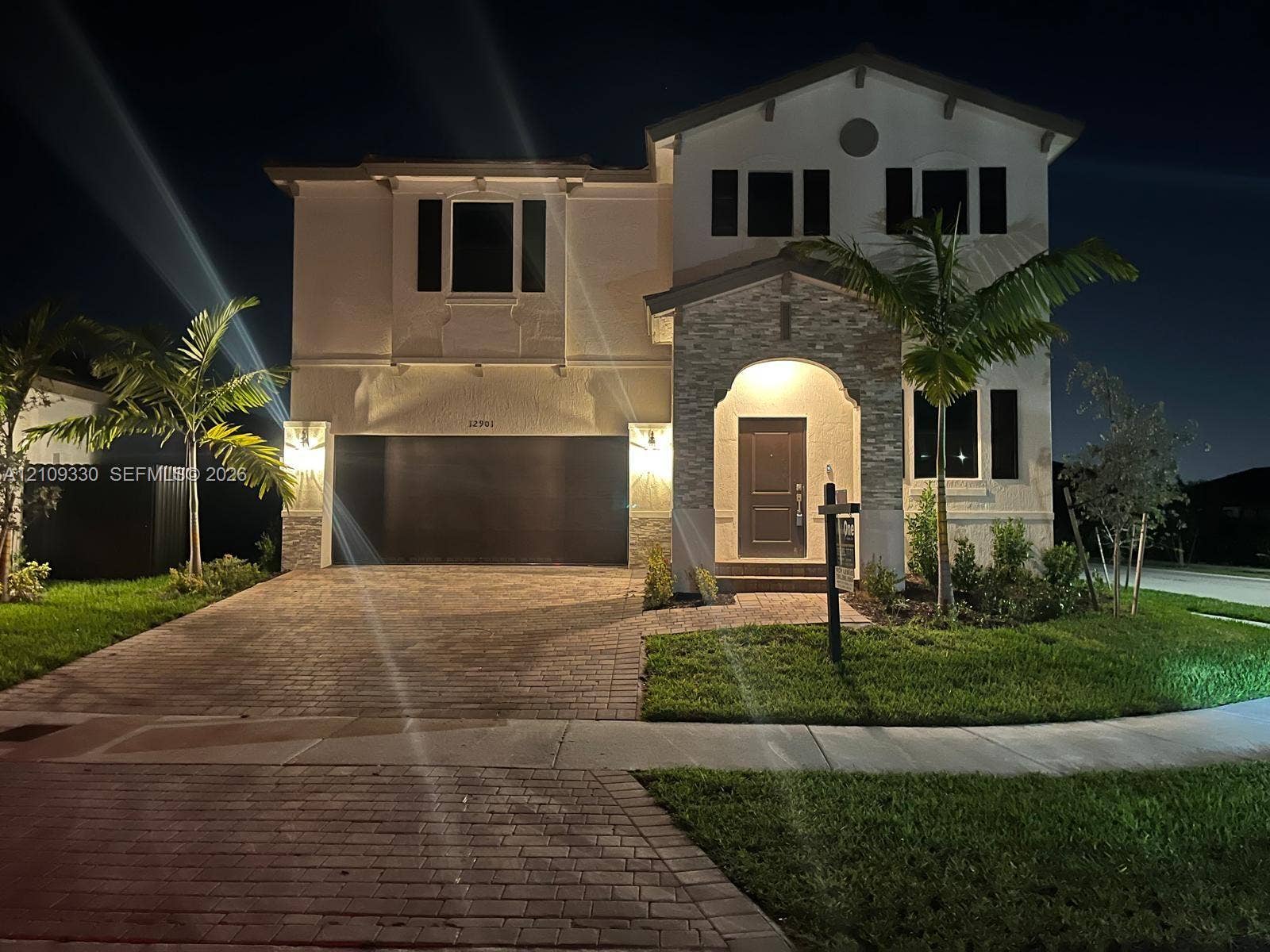 Two-story residence featuring a stucco facade, stone-veneer entryway, arched covered porch, and paved driveway