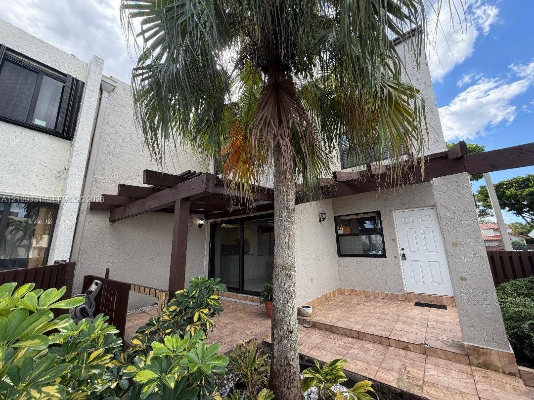 10231 Fontainebleau Boulevard, #106, Miami, FL 33172 Stucco exterior featuring a timber pergola, tiled patio, sliding glass door, and integrated outdoor lighting