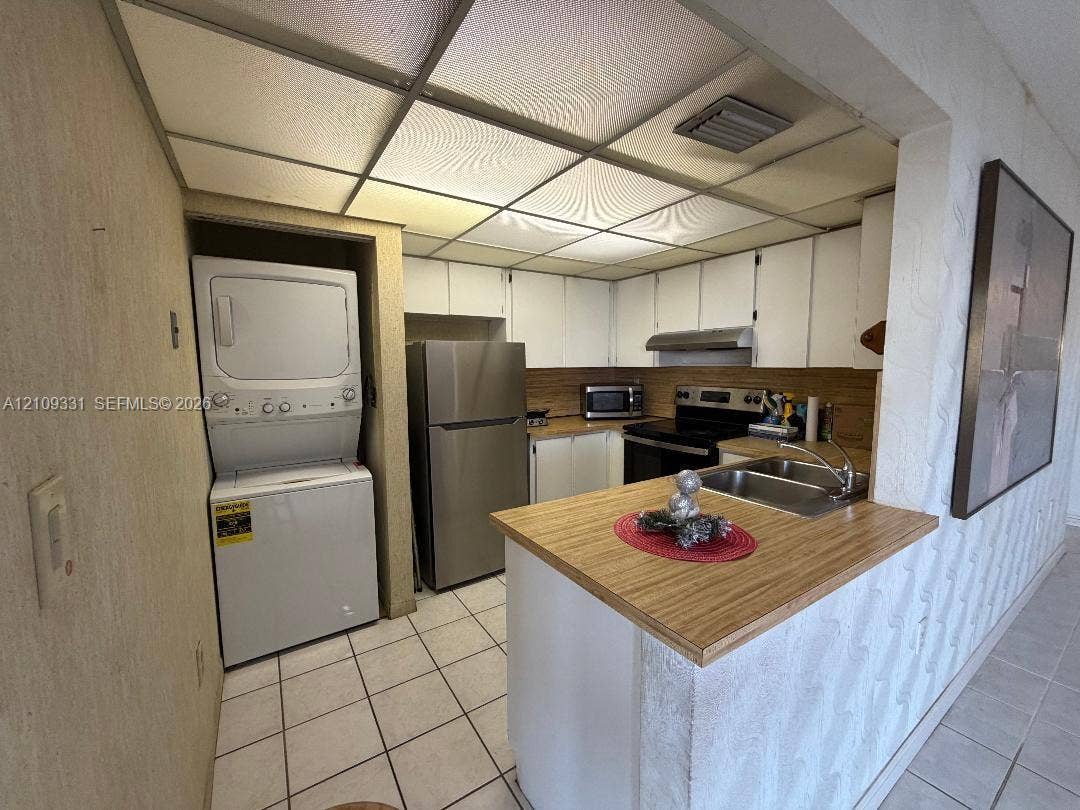 10231 Fontainebleau Boulevard, #106, Miami, FL 33172 Kitchen featuring white cabinetry, wood-finish countertops, stainless steel appliances, a double-basin sink, and integrated laundry unit