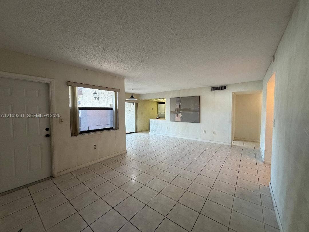 10231 Fontainebleau Boulevard, #106, Miami, FL 33172 Open-concept interior featuring neutral ceramic tile flooring, a breakfast bar with stone-surface countertop, and a window with a horizontal blind