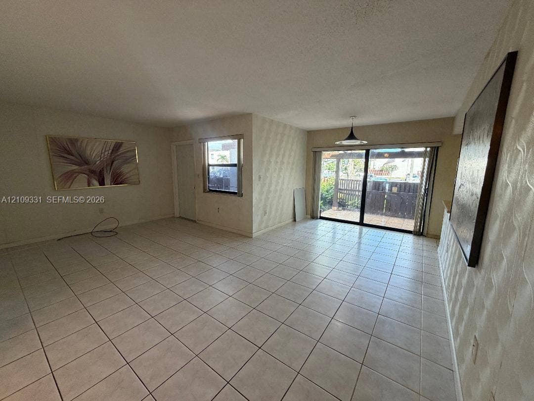 10231 Fontainebleau Boulevard, #106, Miami, FL 33172 Neutral-toned interior featuring ceramic tile flooring, textured wall accents, a pendant light fixture, and sliding glass doors with exterior access