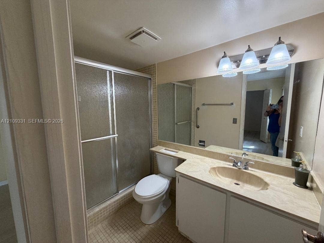 10231 Fontainebleau Boulevard, #106, Miami, FL 33172 Bathroom featuring a glass-enclosed shower, stone-surfaced vanity with an integrated oval sink, and a full-width vanity mirror with integrated three-bulb lighting