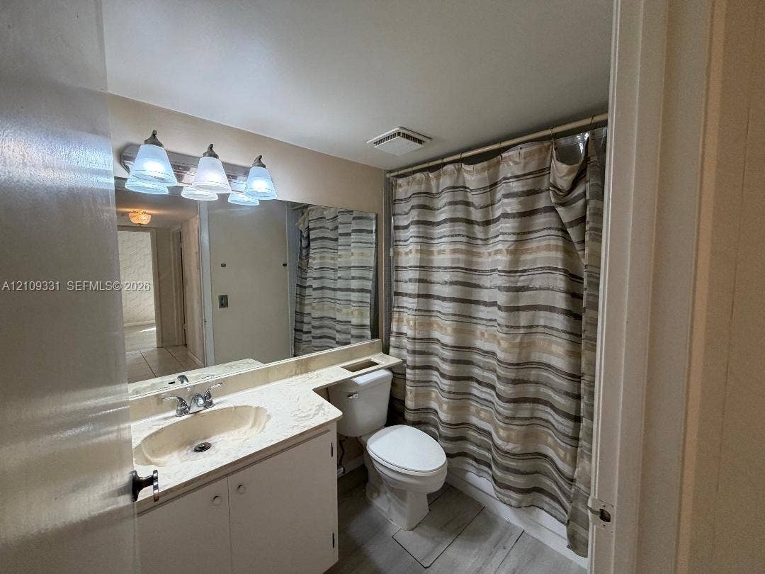 10231 Fontainebleau Boulevard, #106, Miami, FL 33172 Bathroom vanity with stone-finish countertop, integrated sink, large wall-mounted mirror, three-light fixture, and wood-finish flooring
