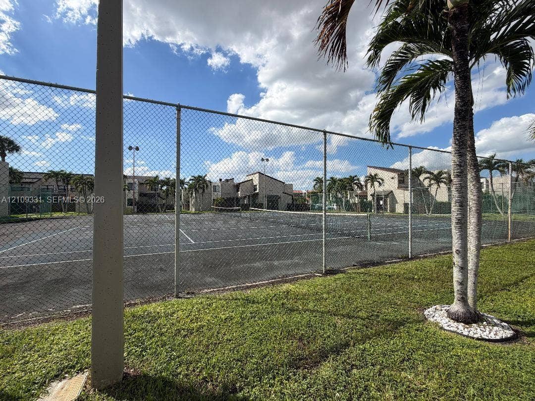 10231 Fontainebleau Boulevard, #106, Miami, FL 33172 Tennis court with a chain-link perimeter fence, integrated lighting, and manicured landscaping
