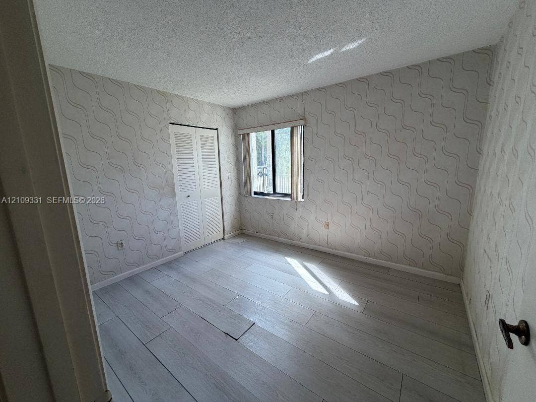 10231 Fontainebleau Boulevard, #106, Miami, FL 33172 Room featuring wood-finish flooring, textured wallpaper, a single window, and dual-panel closet doors