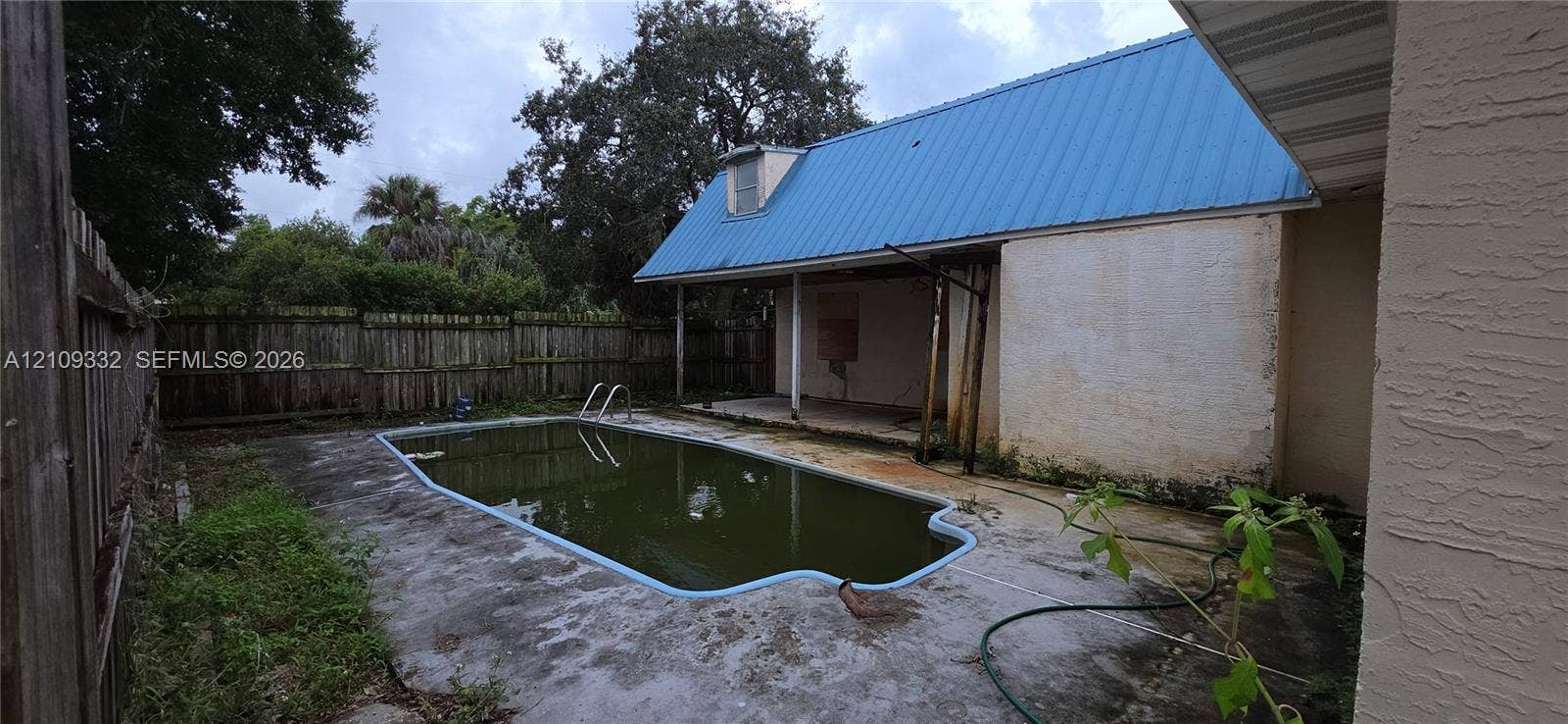 In-ground swimming pool with concrete decking, blue metal roof, and wood privacy fencing