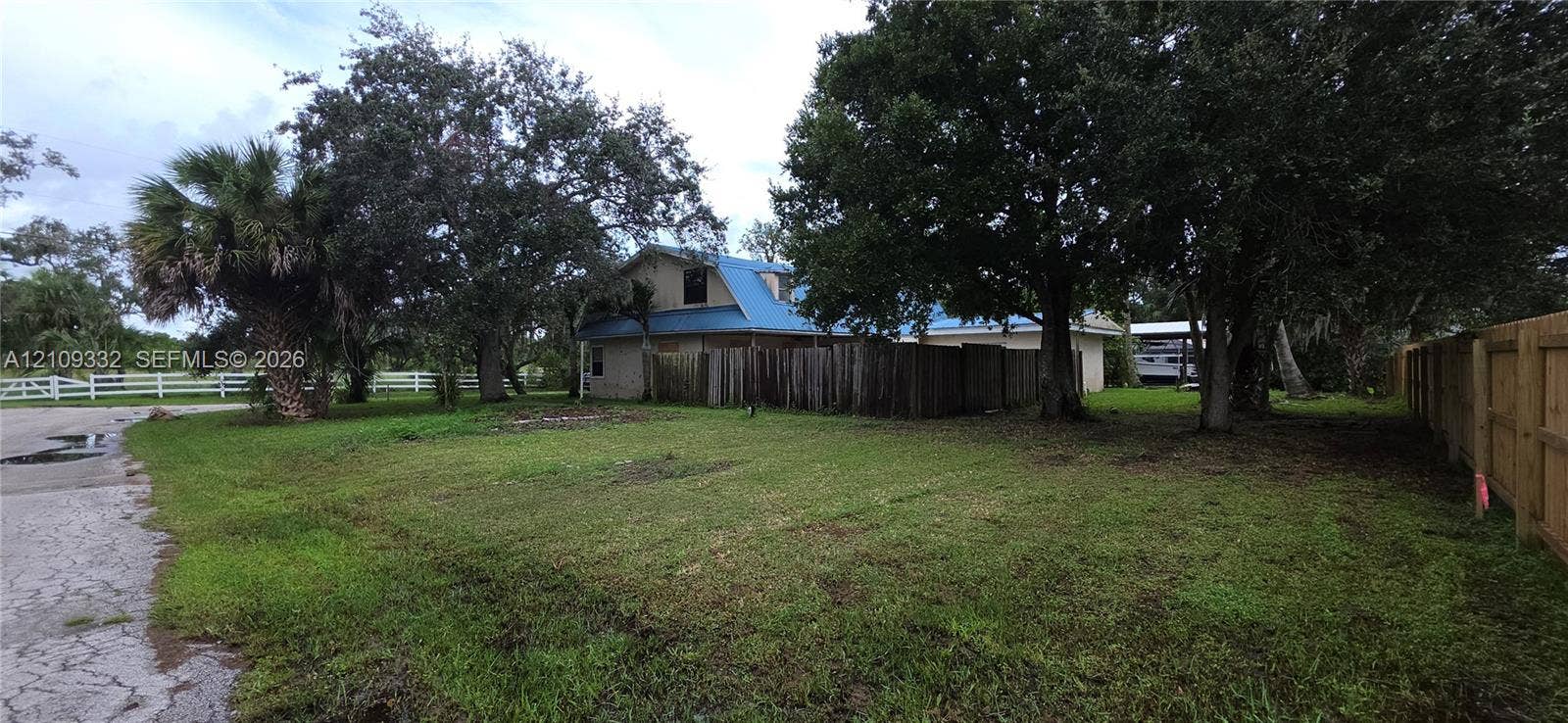 Expansive grounds featuring mature oak trees, established palms, wood fencing, and metal roofing