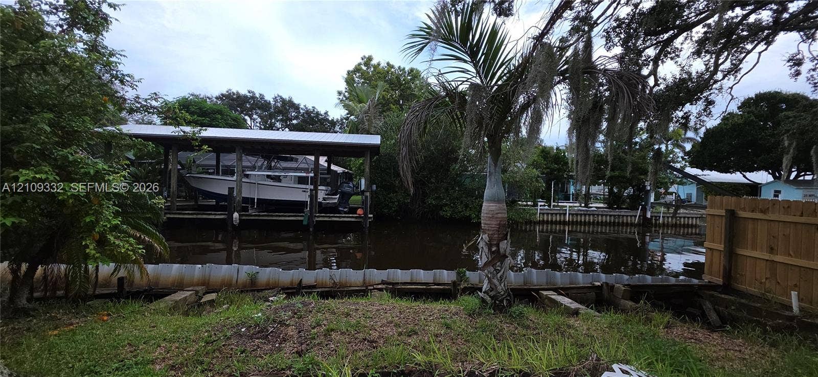 Waterfront property featuring a private covered boat lift, bulkhead seawall, and mature tropical landscaping