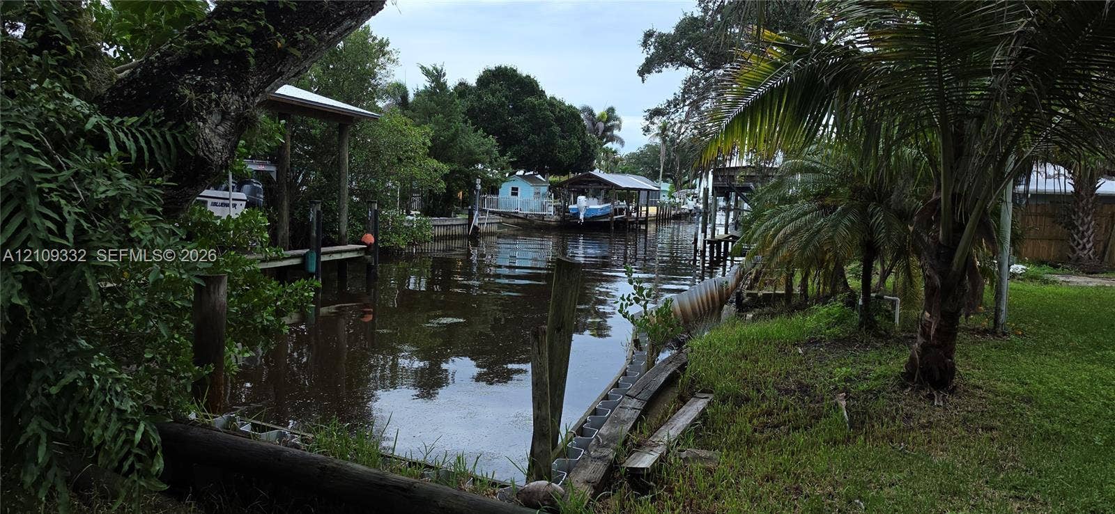 Waterfront property featuring a private boat dock, covered boat slip, bulkhead, and mature tropical landscaping