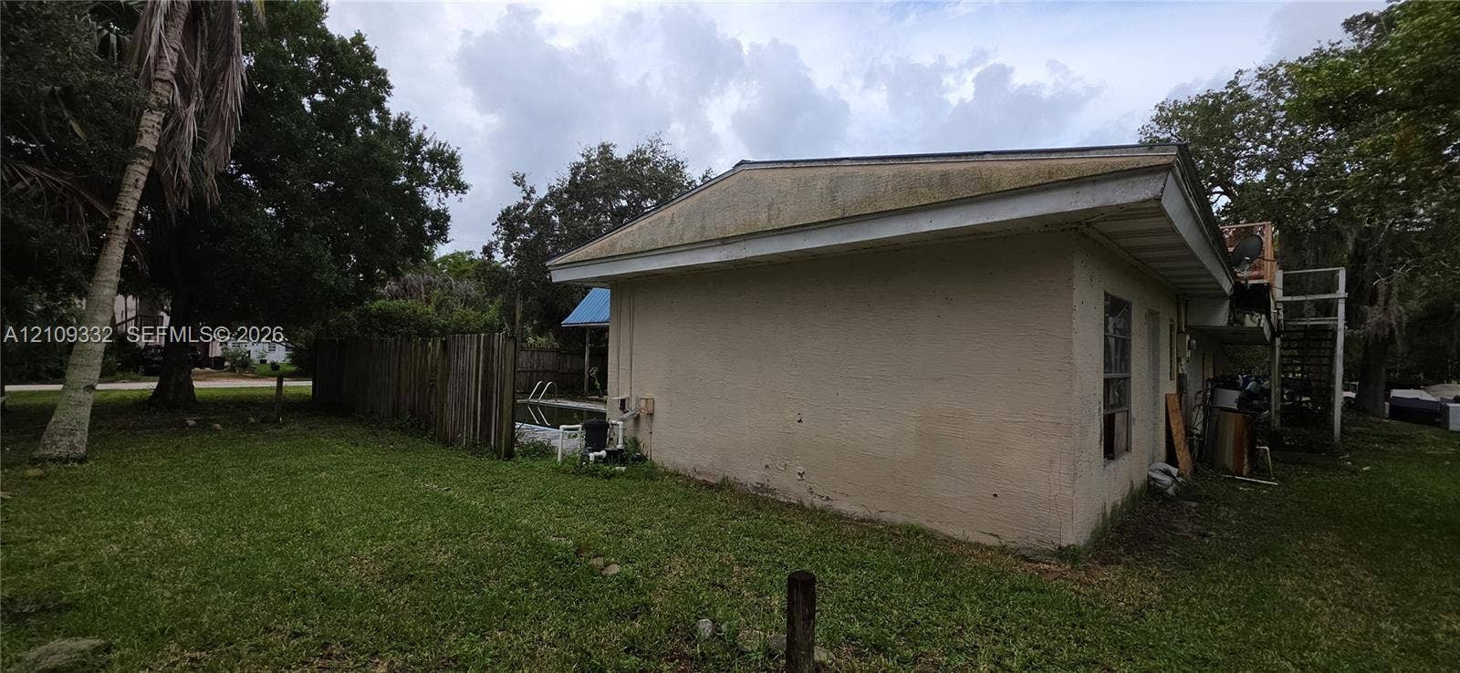 Stucco exterior, in-ground swimming pool, wood-plank fencing, and mature trees on the lot