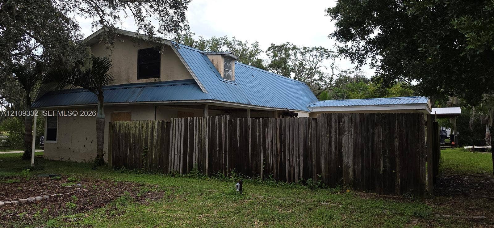 Two-story exterior featuring a metal roof, dormer window, and wood-panel privacy fencing