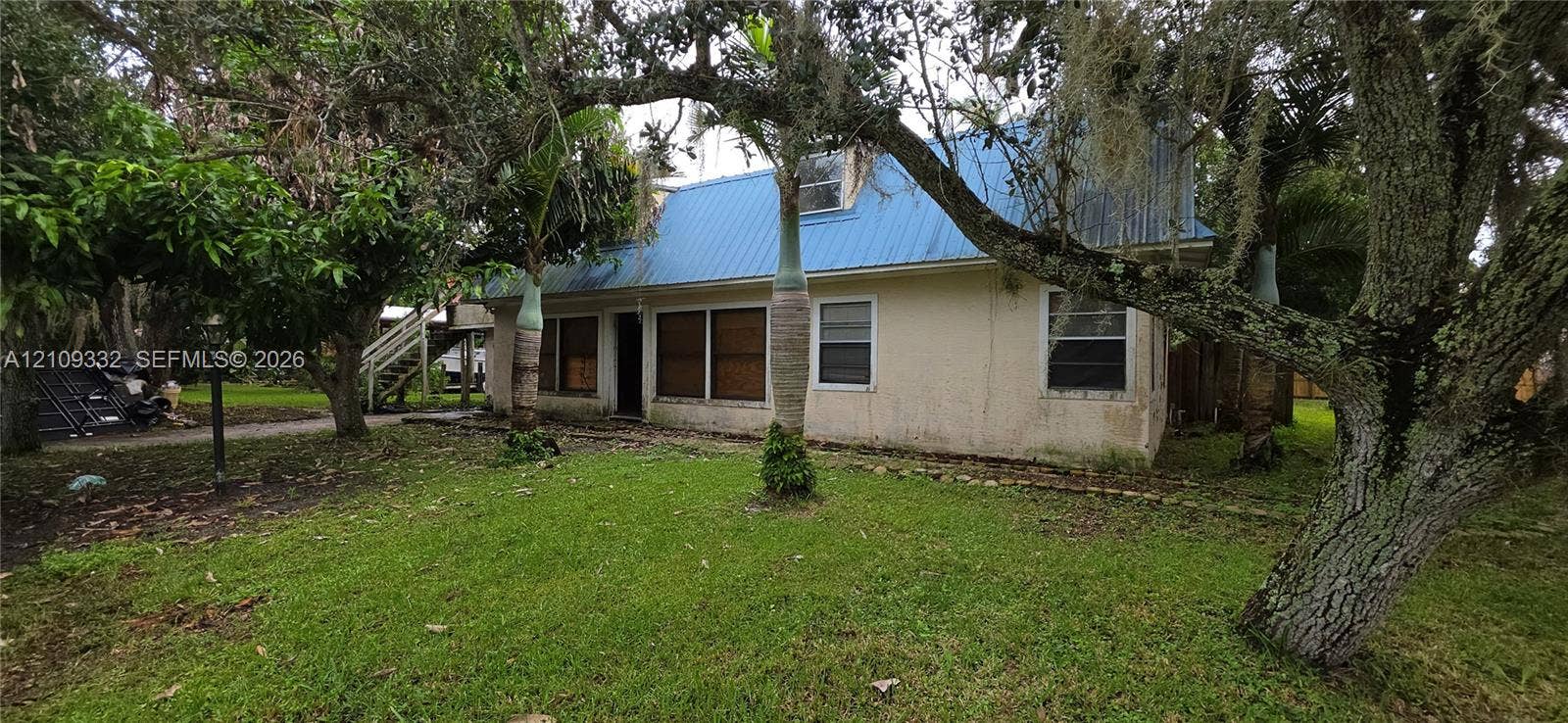 Stucco exterior residence featuring a blue metal roof, grass lawn, and mature canopy trees