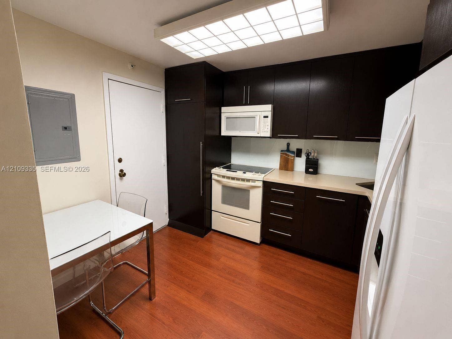 Kitchen featuring dark-finish cabinetry, solid-surface countertops, wood-finish flooring, integrated refrigeration, and a flush-mount grid ceiling light
