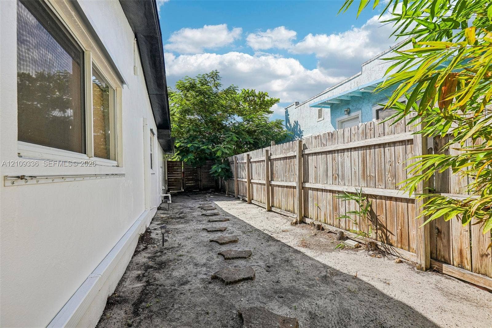 Side yard featuring a smooth stucco exterior finish, horizontal wood fencing, and concrete paver stepping stones