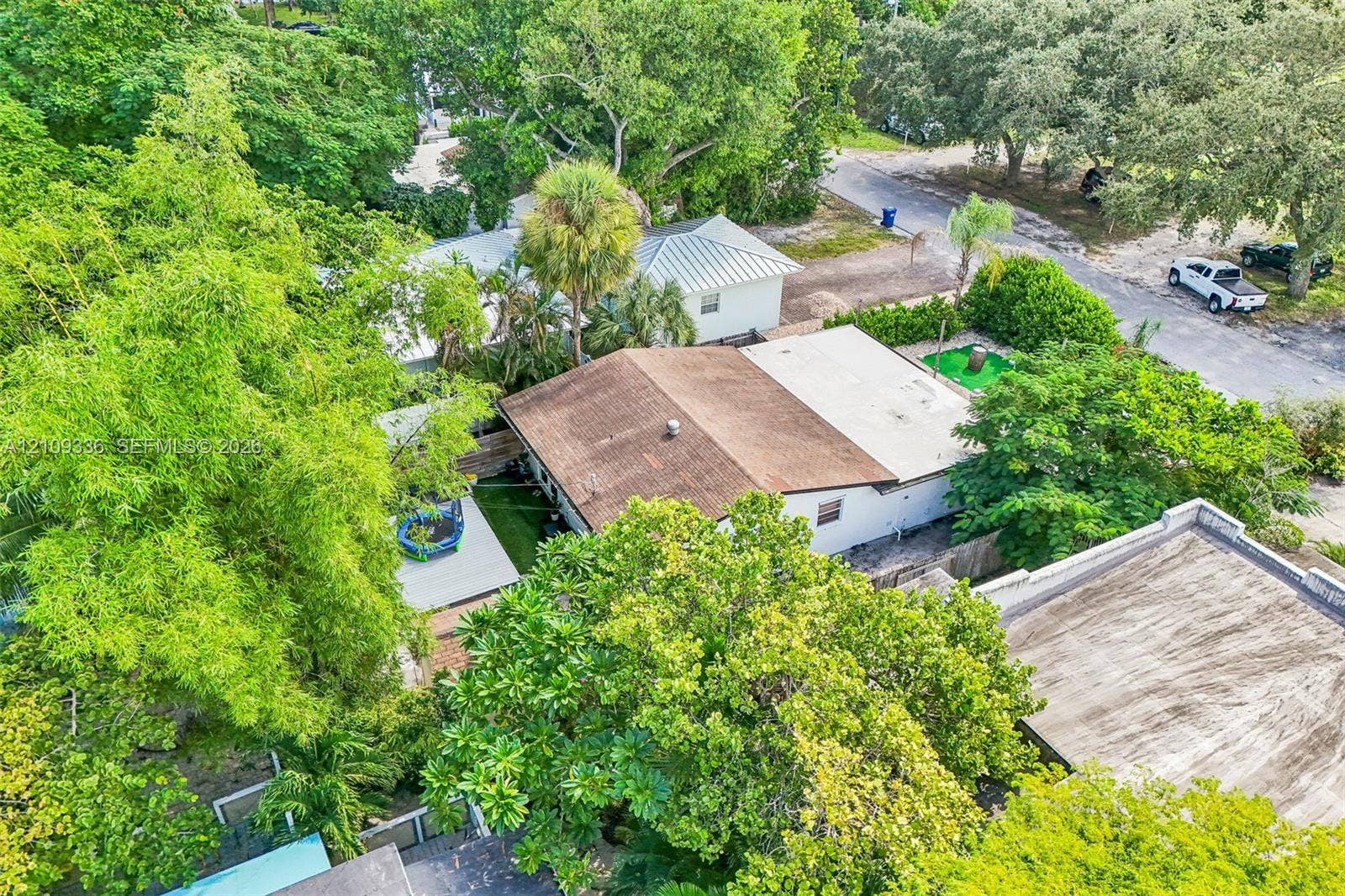 Aerial perspective of a property featuring a composition shingle roof, mature landscaping, established trees, and a wooden deck
