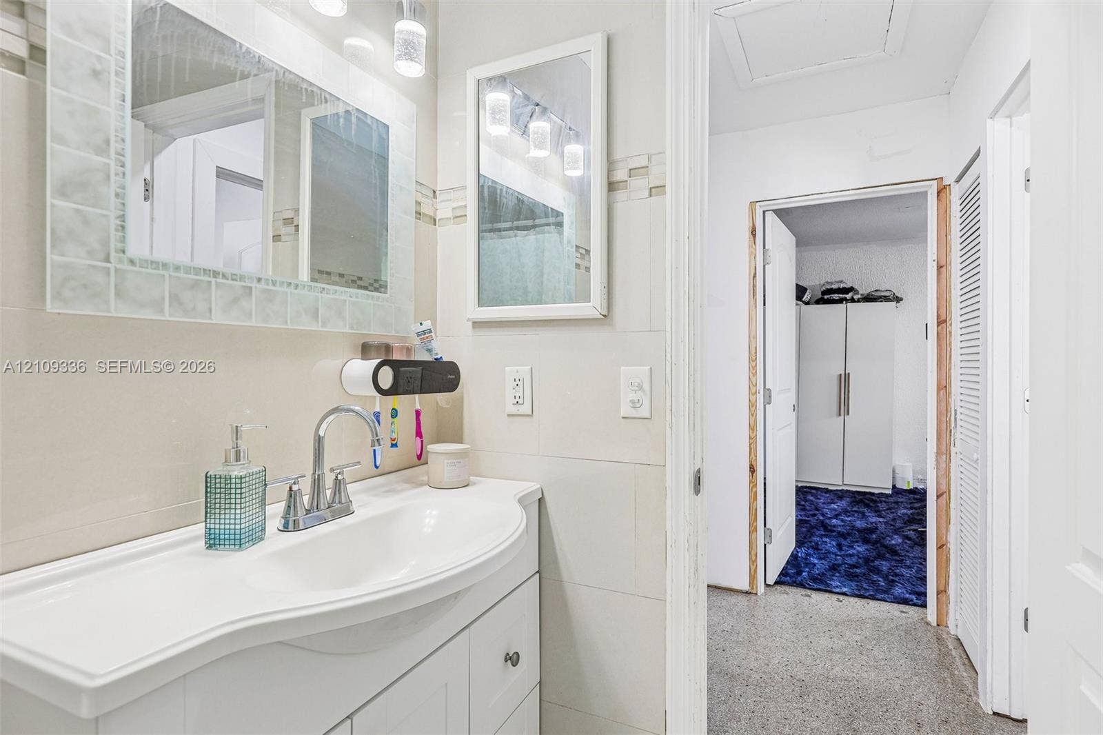 Bathroom vanity featuring an integrated basin, chrome faucet, wall-mounted mirror, and decorative tile backsplash