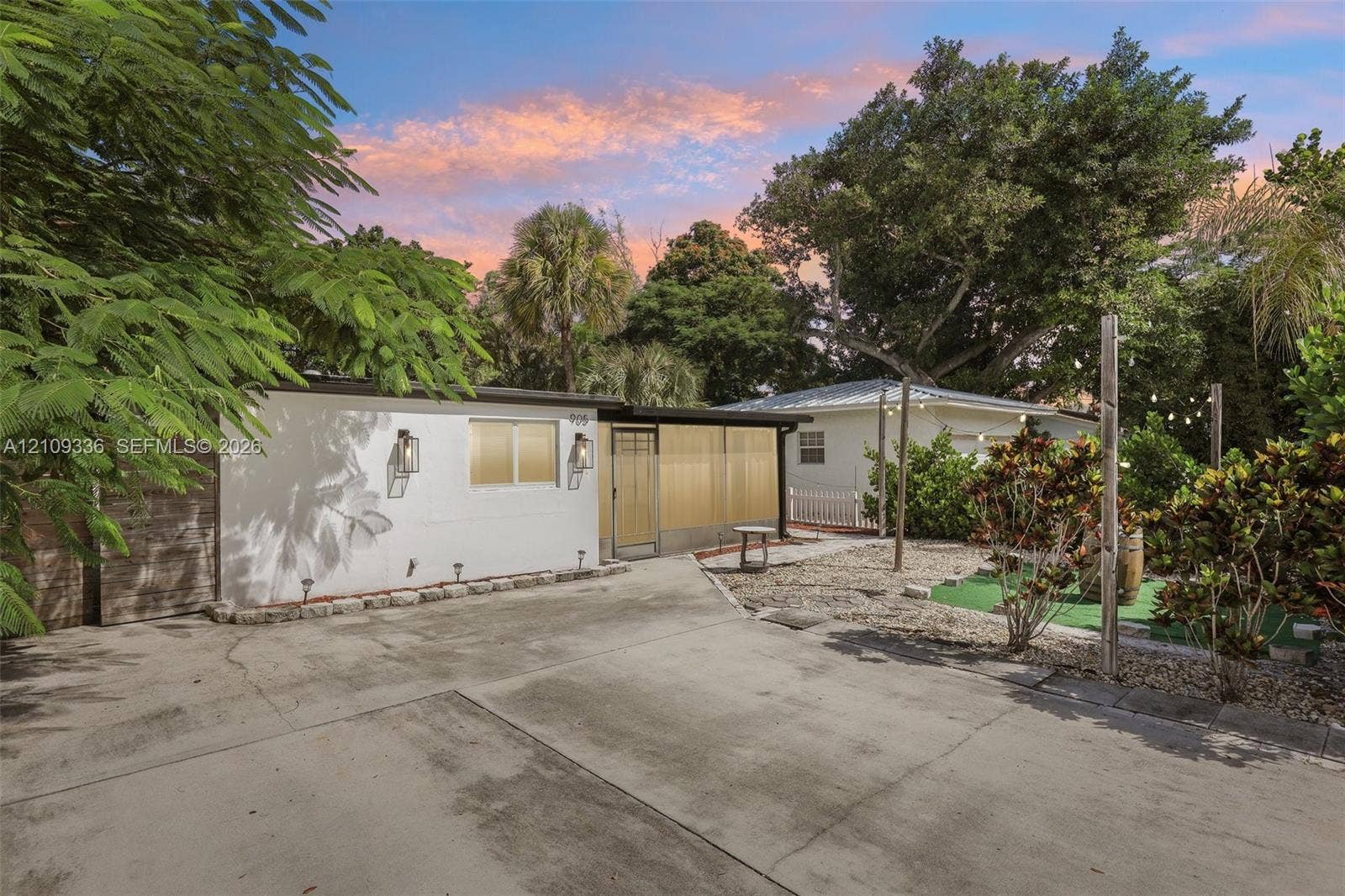 Exterior featuring a concrete driveway, metal-framed screened entryway, wall-mounted exterior lighting, and gravel landscaping