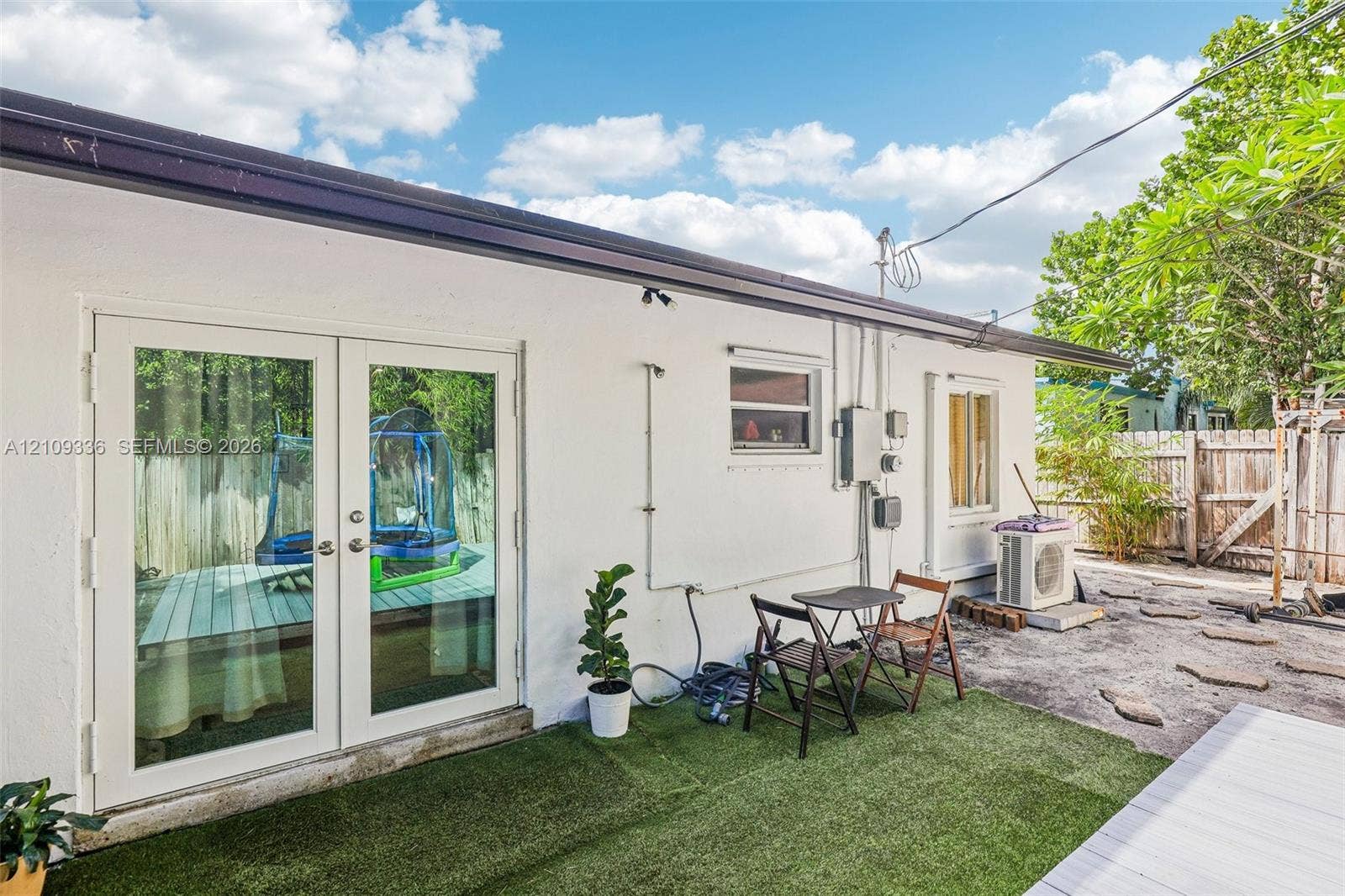 Exterior wall featuring white smooth stucco finish, double French doors with glass panes, and a dedicated outdoor heating and cooling unit