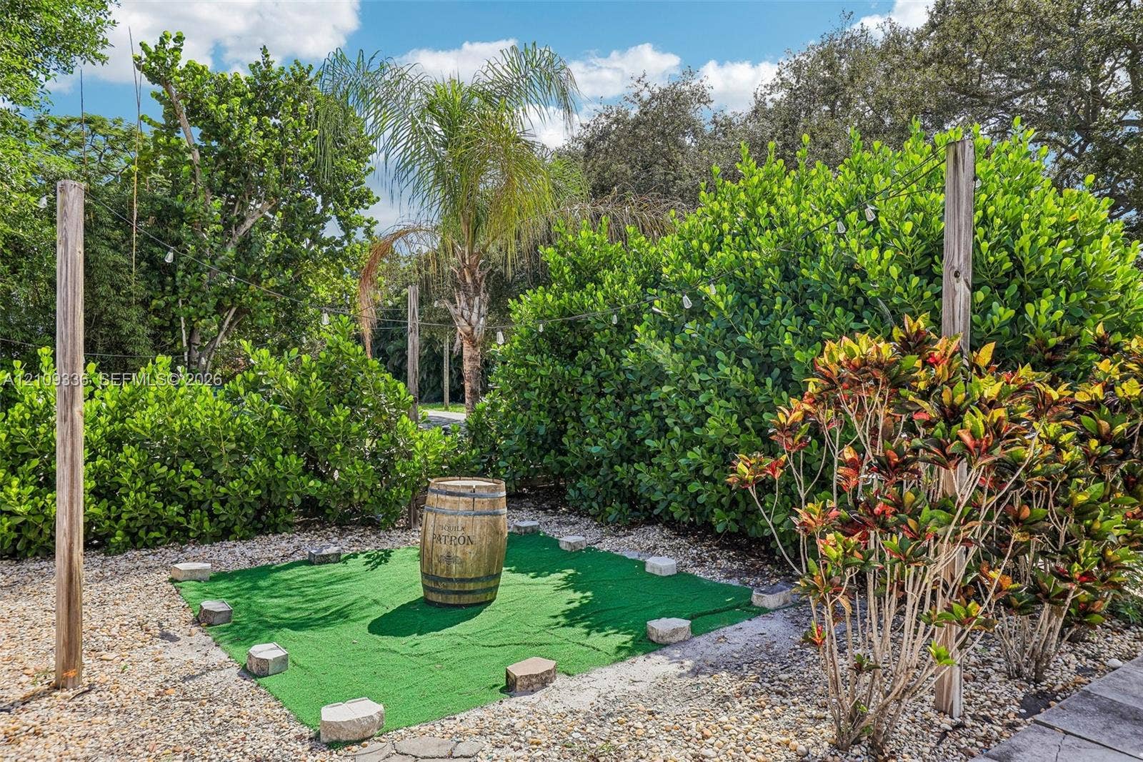 Outdoor area featuring synthetic turf, decorative stone border, perimeter string lighting, and mature tropical landscaping