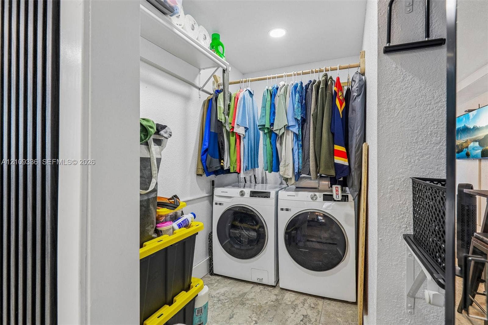 Laundry area featuring white front-loading washer and dryer, integrated overhead shelving, a dedicated garment rod, and tile flooring