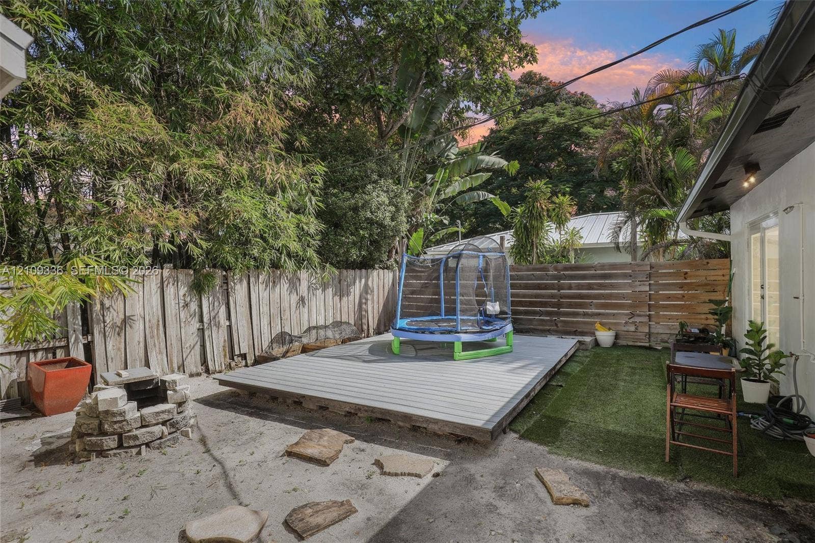 Private backyard featuring a raised composite deck, stone-constructed fire pit, horizontal wood fencing, and synthetic grass turf