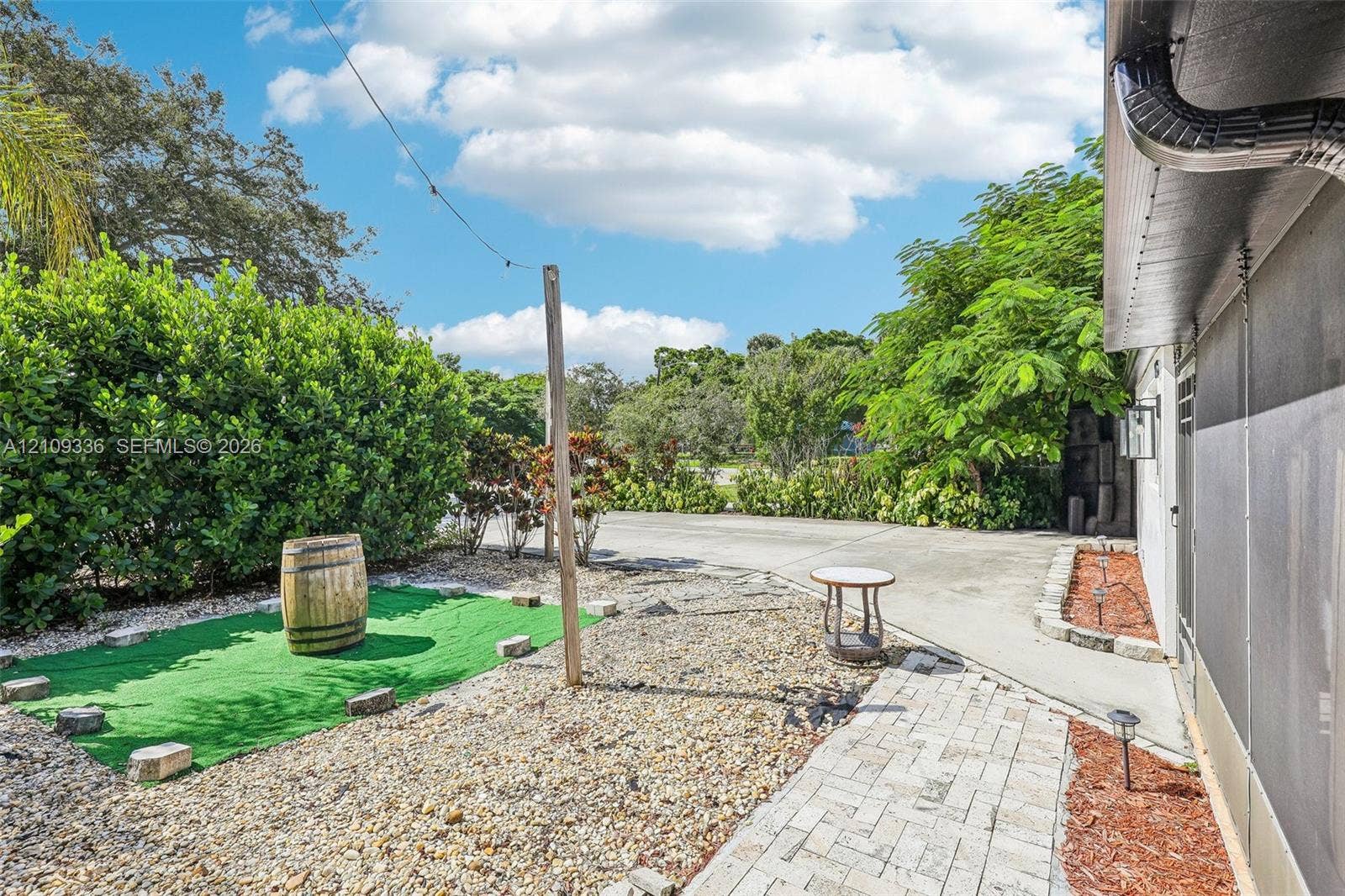 Outdoor space featuring a paved walkway, gravel ground cover, and mature perimeter landscaping