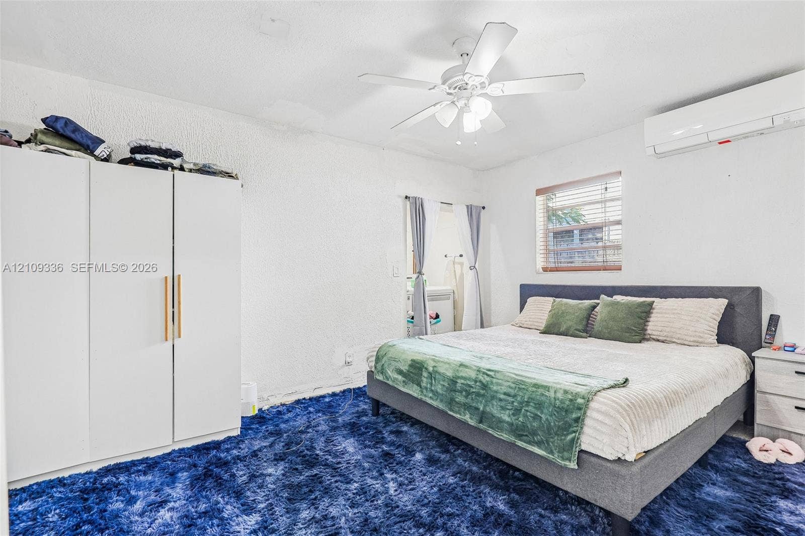 Room featuring a wall-mounted ductless air conditioning unit, ceiling fan with integrated light fixture, and window with slatted blinds