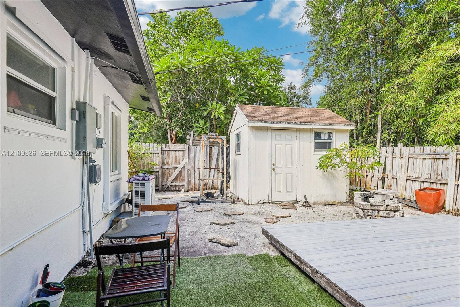 Rear exterior featuring a wood-finish deck, detached storage shed, privacy fencing, and stone hardscaping