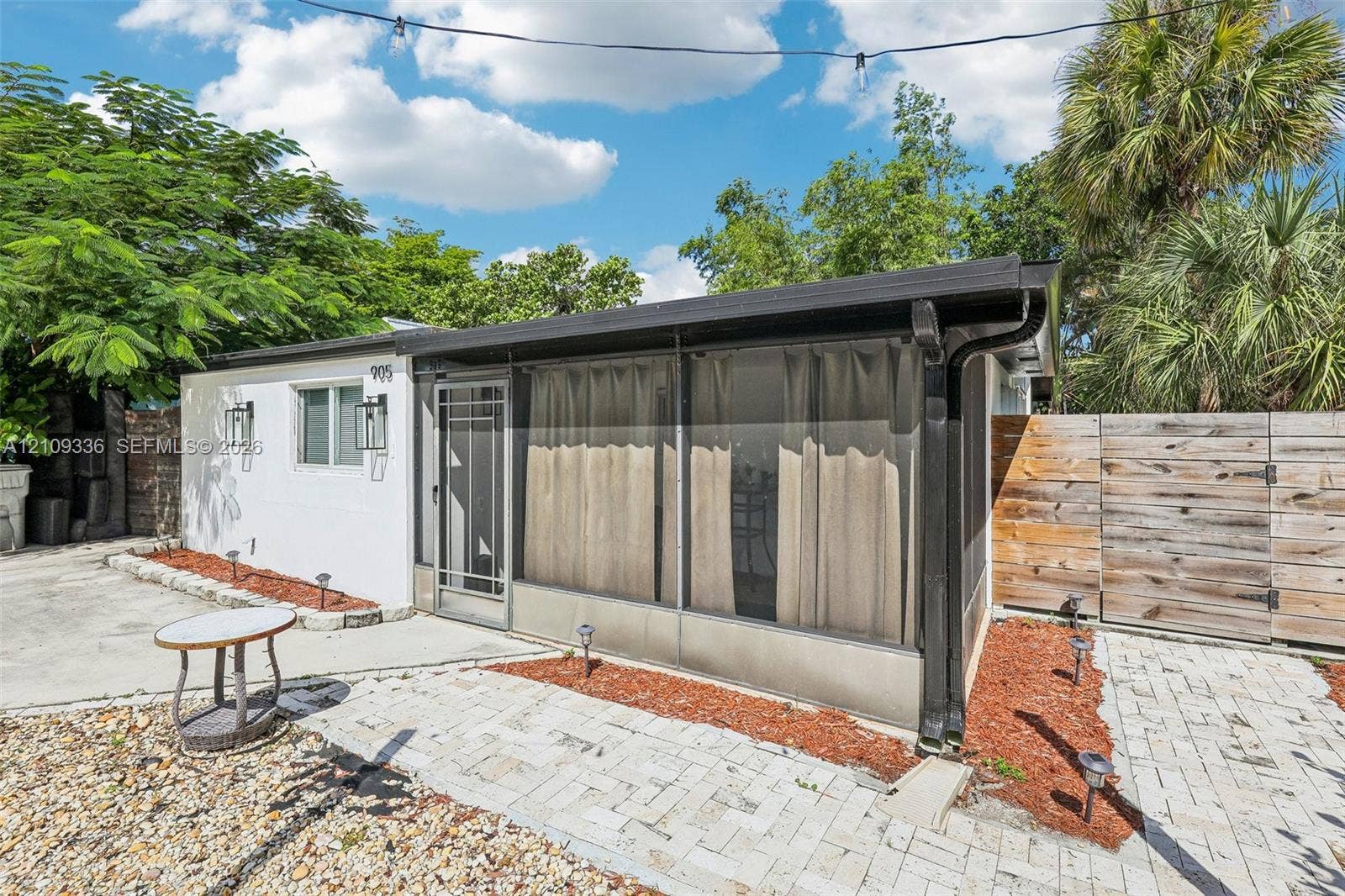 Exterior facade featuring white siding, a screened-in enclosure, concrete paver patio, and horizontal wood-panel fencing