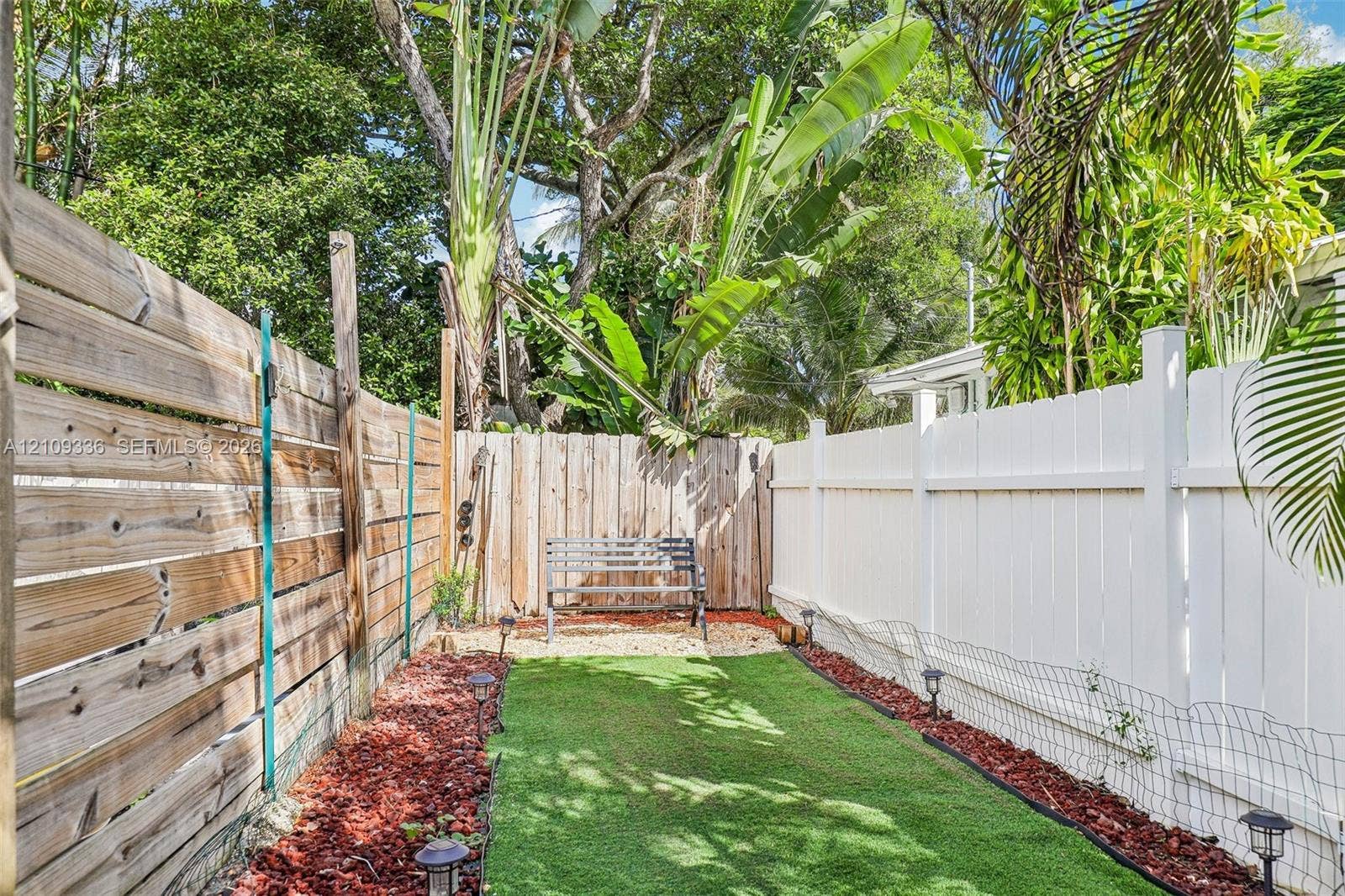 Outdoor area featuring a synthetic turf lawn, wood-slat privacy fencing, vinyl privacy fencing, and stone-accented ground cover