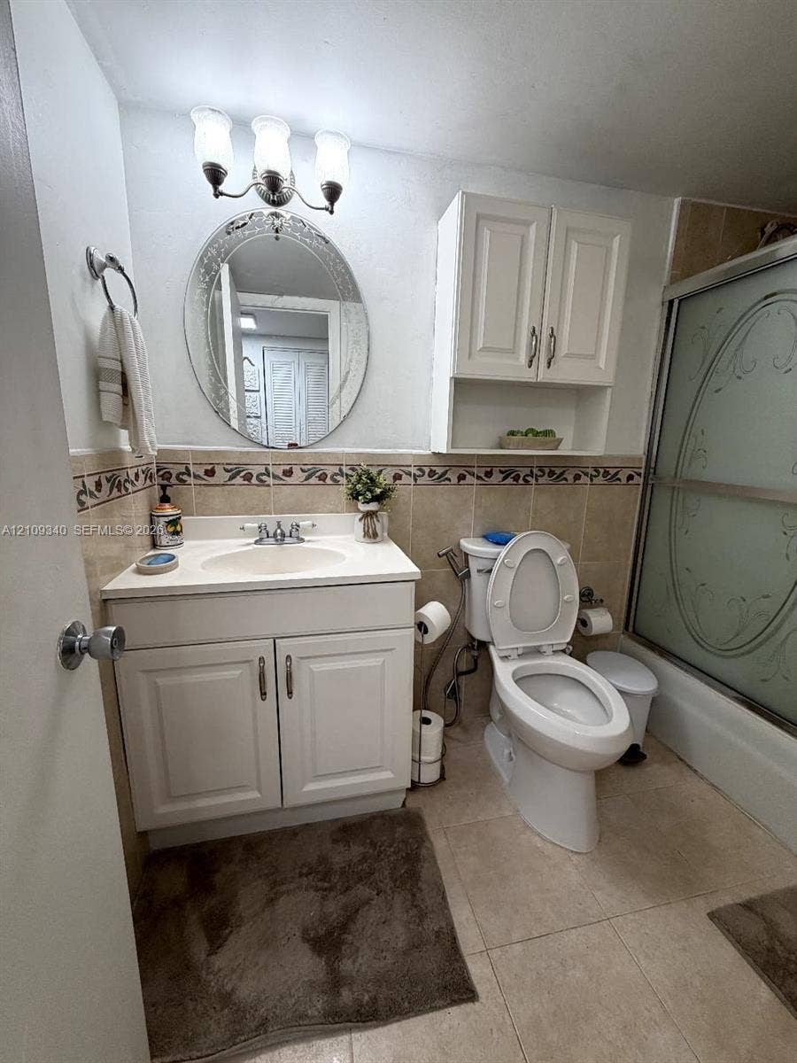 Bathroom featuring a white vanity cabinet with a light-toned countertop, wall-mounted storage cabinetry, a decorative oval mirror, and a three-light fixture