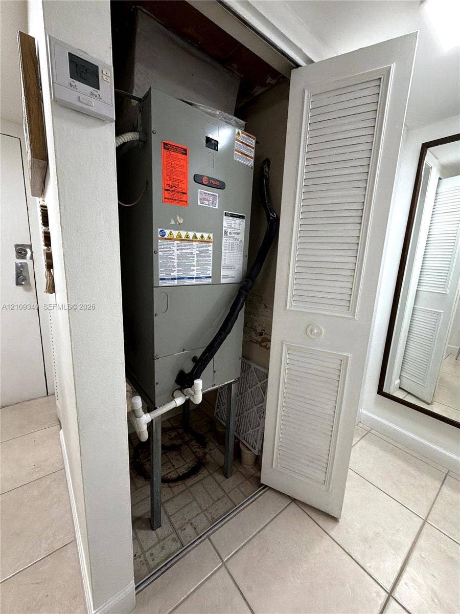 Utility closet containing a central heating and cooling unit with louvered bi-fold door access and programmable digital wall-mounted thermostat