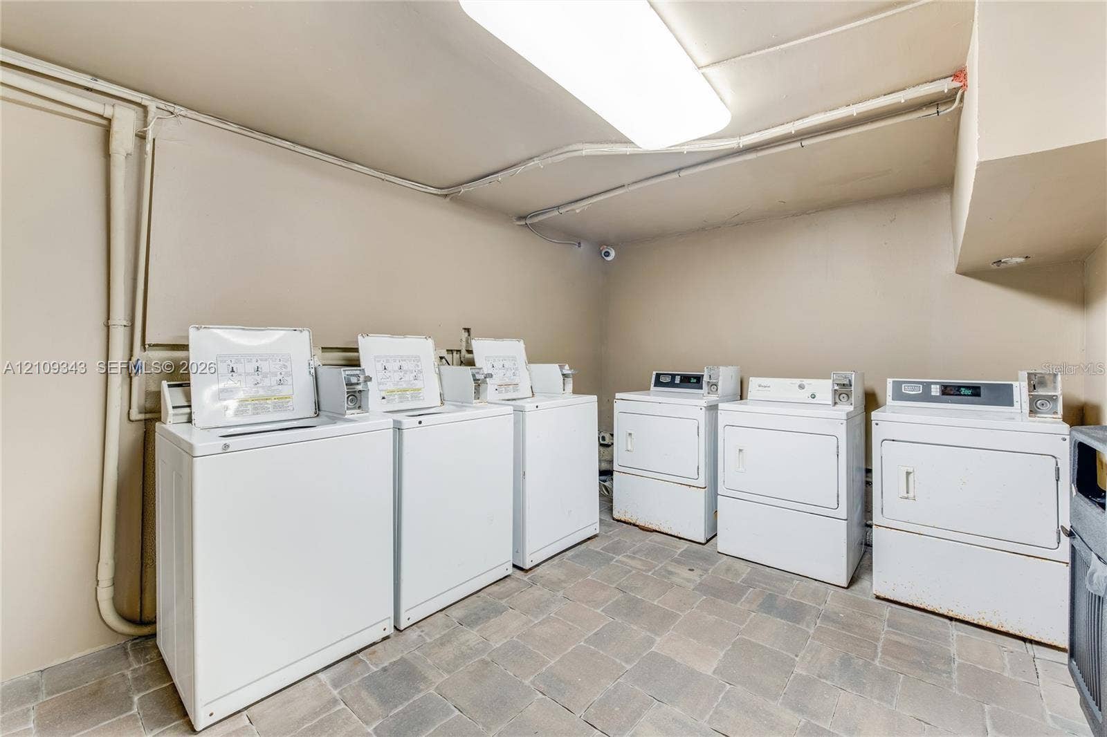 Utility room featuring a multi-unit laundry configuration with three top-load washers and three front-load dryers, complemented by stone-finish tile flooring