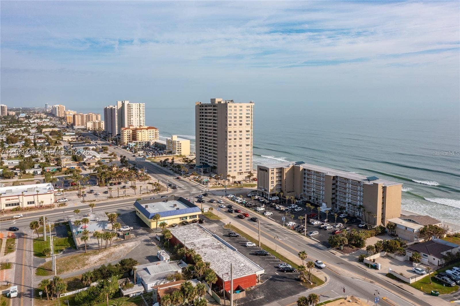 Aerial perspective of coastal landscape featuring direct oceanfront positioning, expansive sandy shoreline, and proximity to major roadways
