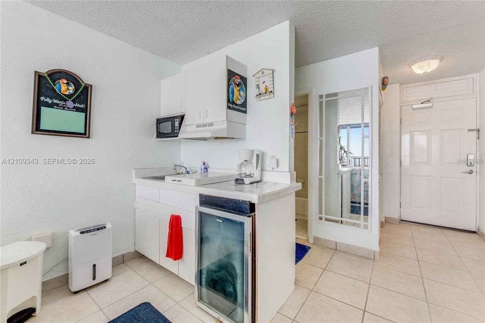 Kitchenette featuring white cabinetry, a built-in microwave, a glass-front beverage cooler, tile flooring, and a decorative mirrored panel