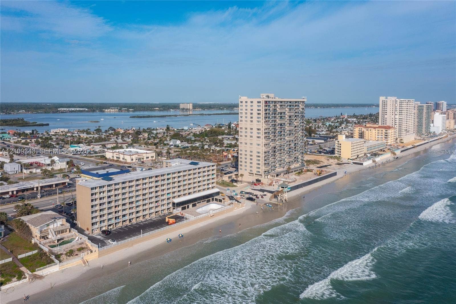 Coastal multi-story building featuring direct shoreline access, paved surface parking, and an exterior swimming pool