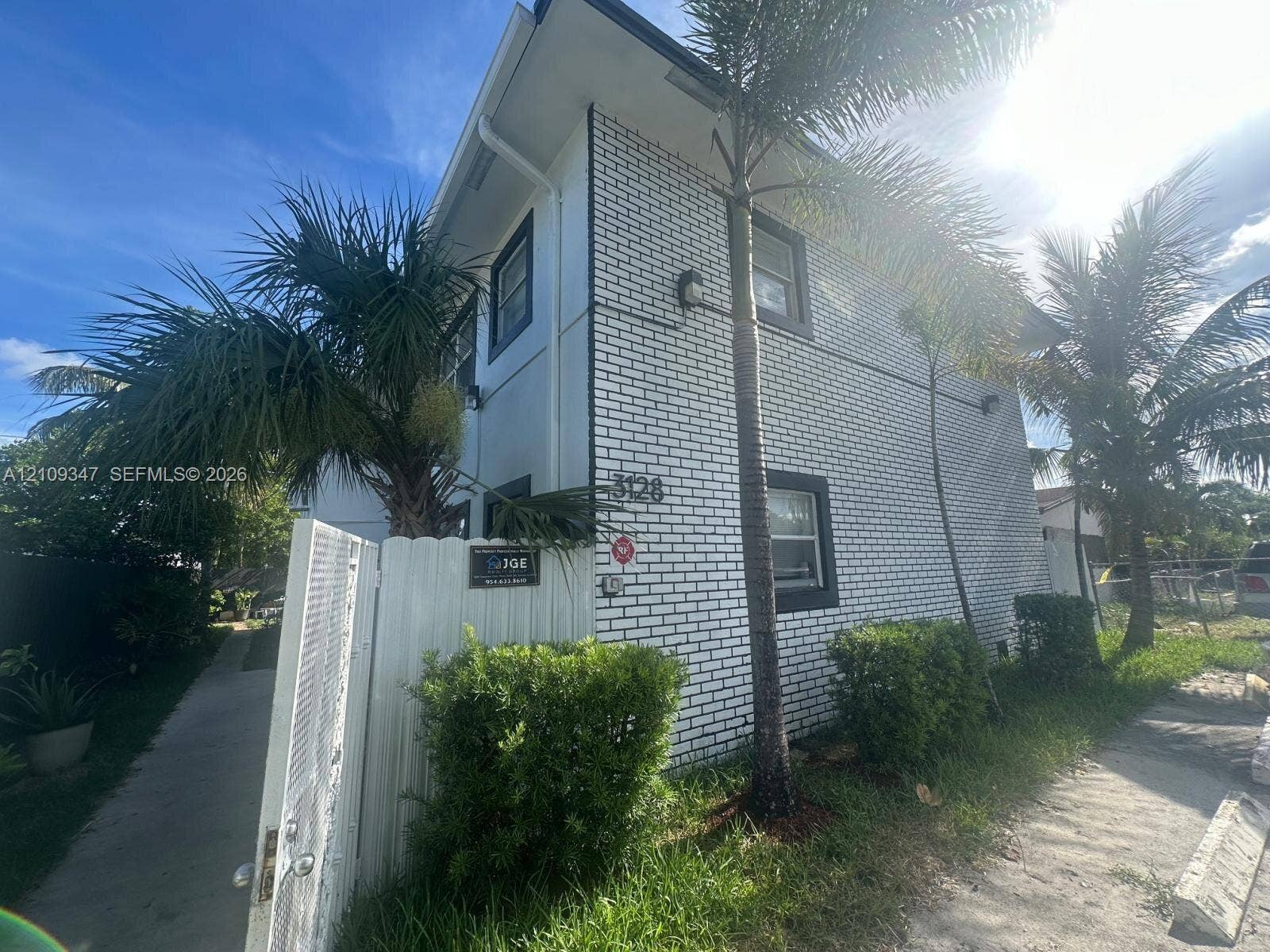 3128 SW 12th Place, #1-4, Fort Lauderdale, Fort Lauderdale, FL 33312 Two-story exterior featuring white brick masonry, dark-trimmed rectangular windows, and a white privacy fence with a gated entrance