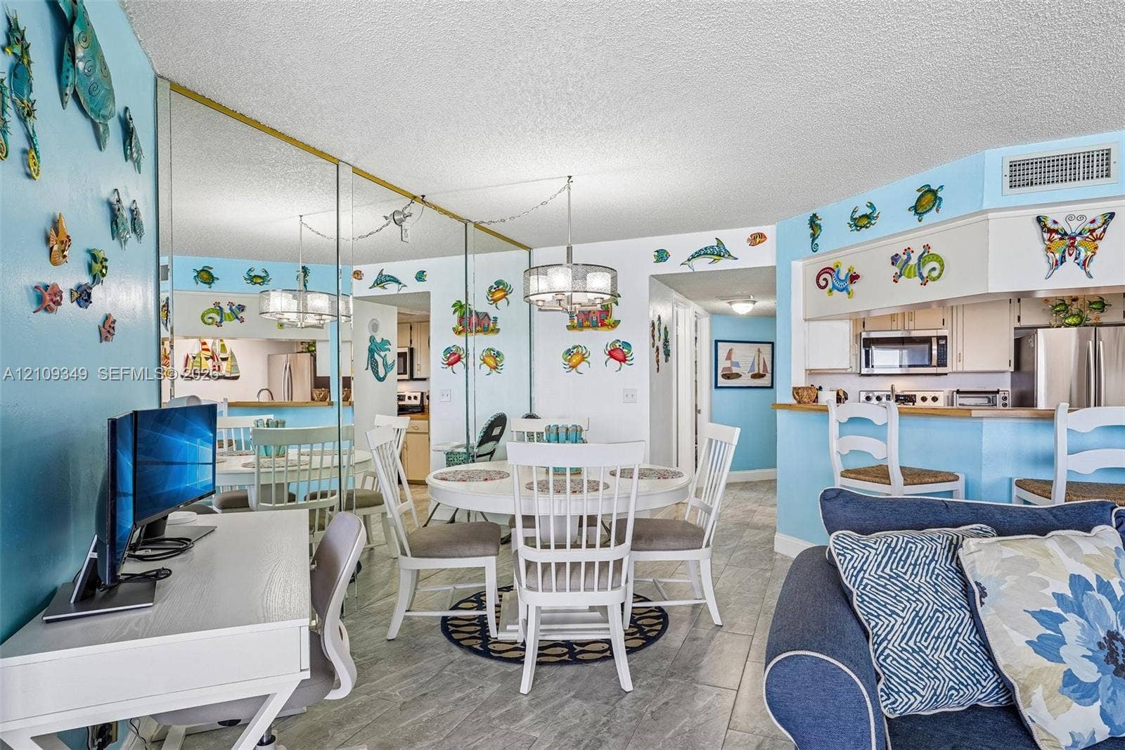 3115 S Atlantic Avenue, #G030, Daytona Beach, FL 32118 Open-concept dining area featuring oversized wall mirrors, neutral tile flooring, multi-light chandeliers, and a breakfast bar