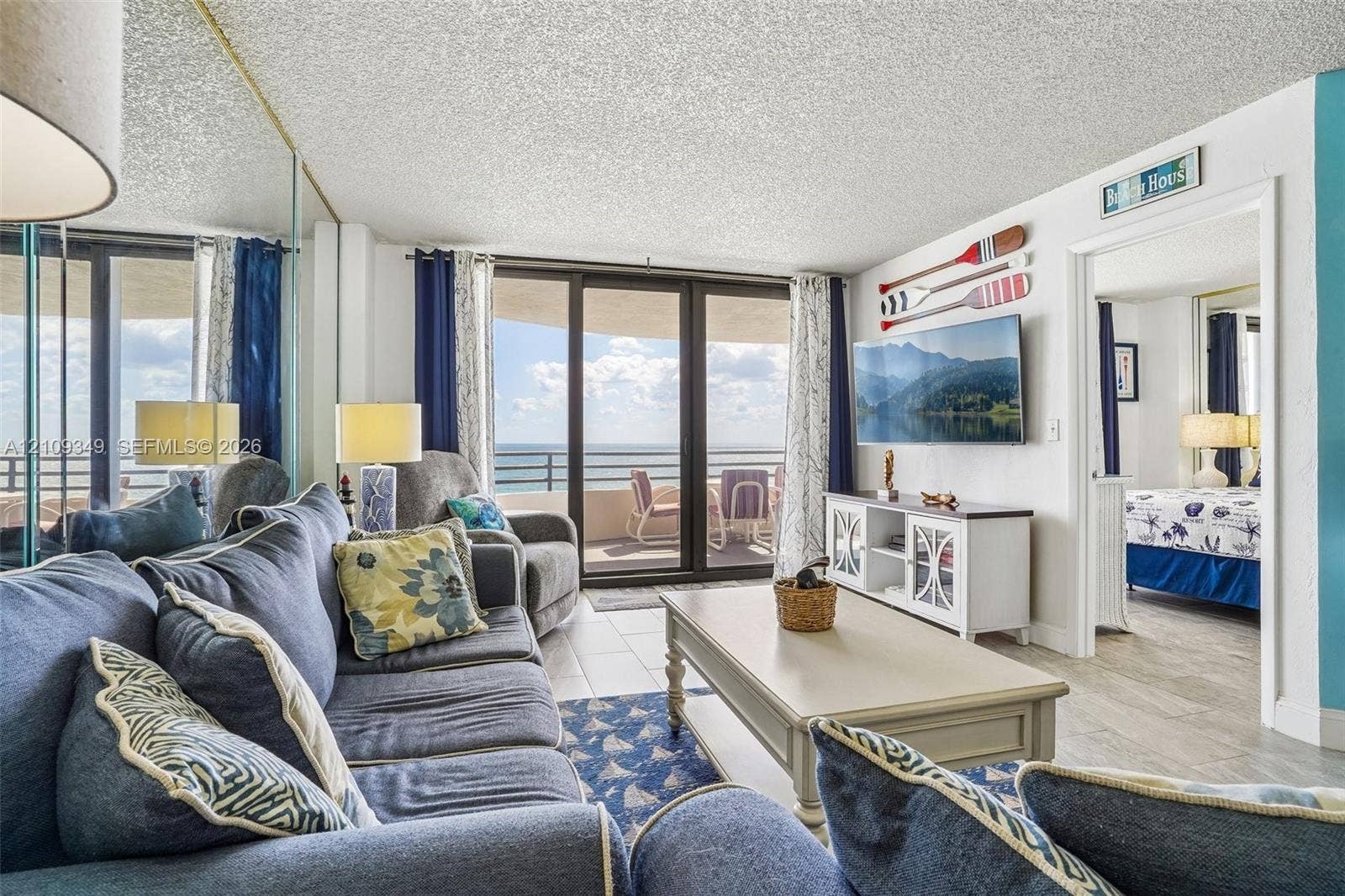 3115 S Atlantic Avenue, #G030, Daytona Beach, FL 32118 Living area featuring tile flooring, floor-to-ceiling mirrored wall panels, and sliding glass doors with access to an exterior balcony