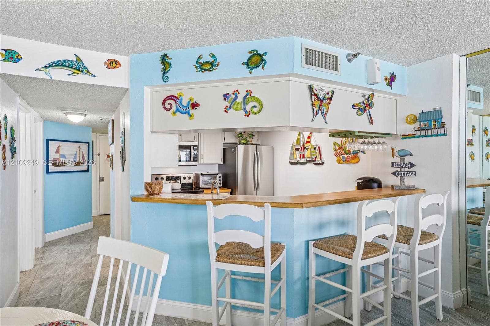 3115 S Atlantic Avenue, #G030, Daytona Beach, FL 32118 Pass-through kitchen featuring stainless steel appliances, light-toned cabinetry, a wood-finish bar counter, and tile flooring