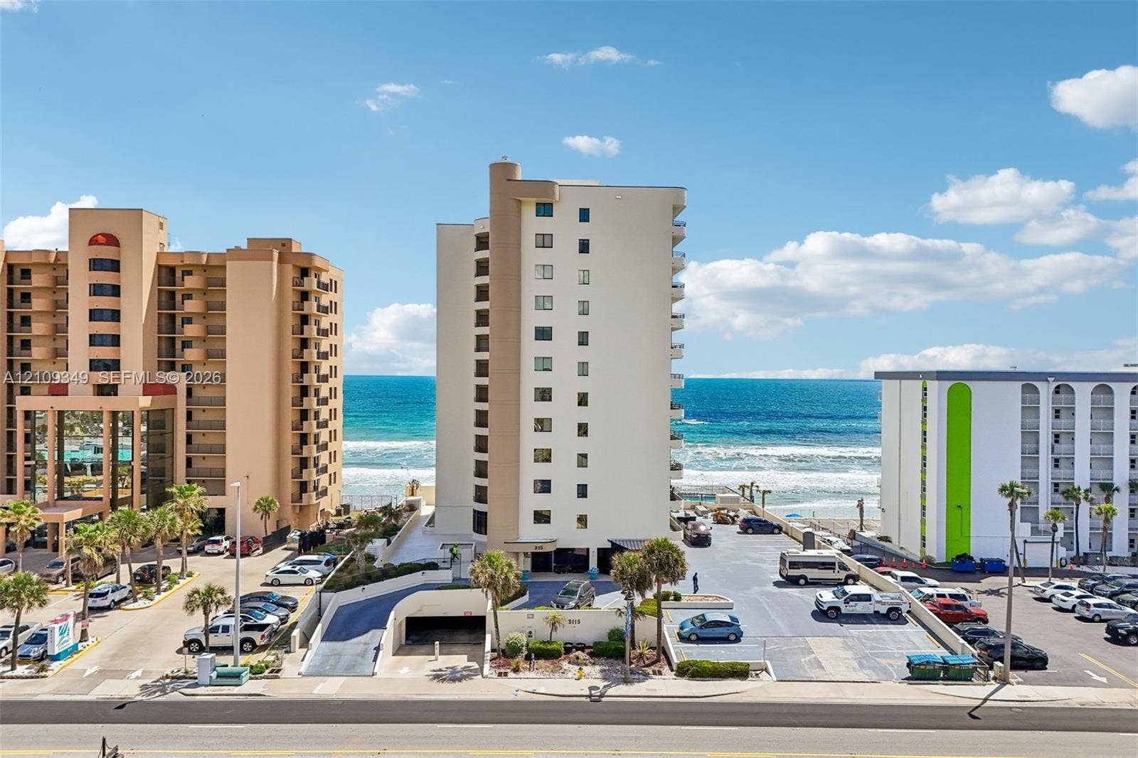 3115 S Atlantic Avenue, #G030, Daytona Beach, FL 32118 High-rise beachfront building featuring a multi-story exterior, paved parking area, ground-level covered parking access, and mature palm trees