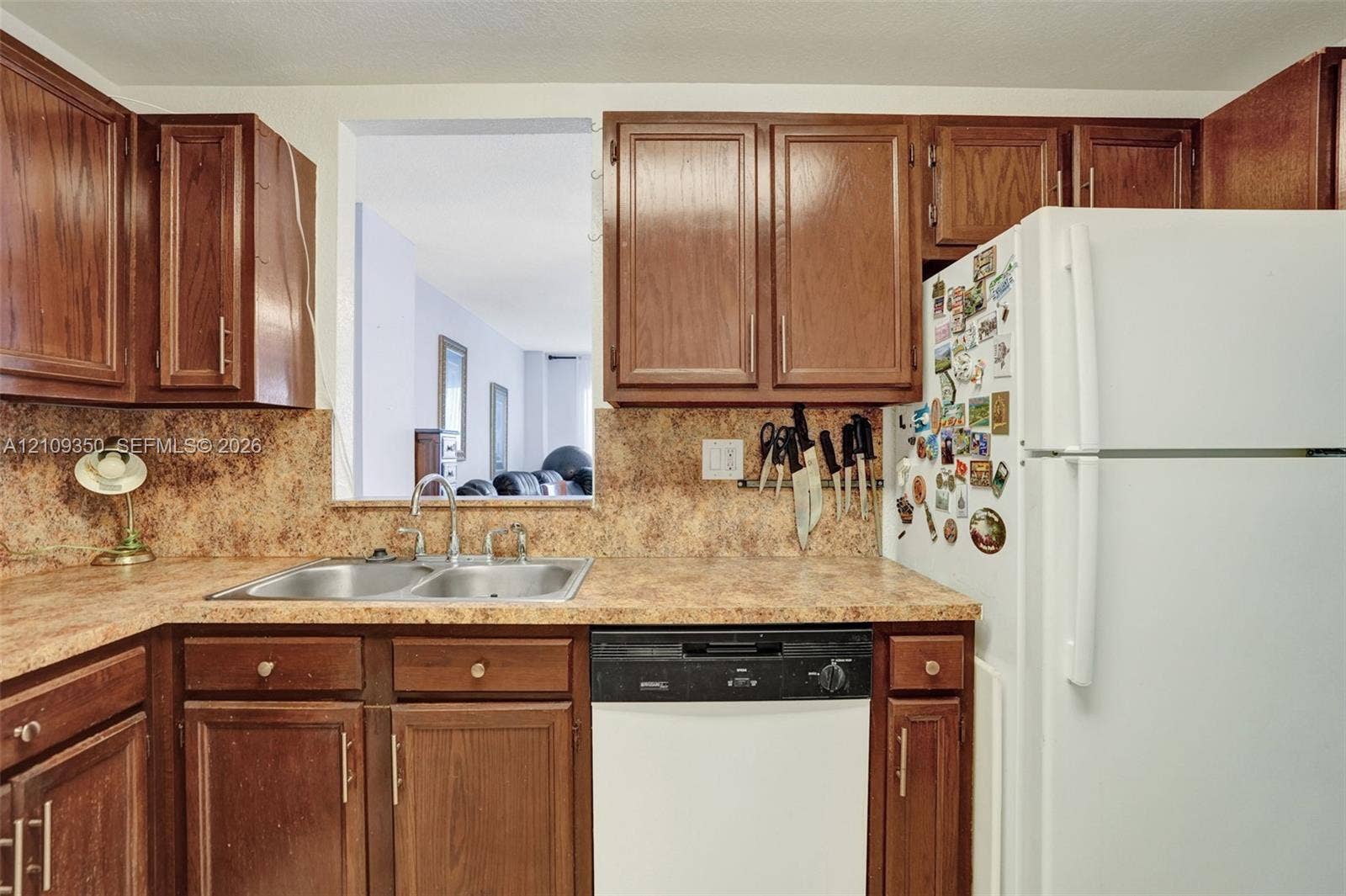 10777 W Sample Road, #616, Coral Springs, FL 33065 Kitchen featuring stained-wood cabinetry, laminate countertops, a dual-basin stainless steel sink, and integrated dishwasher