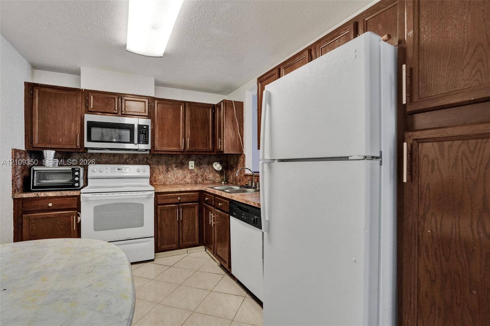 10777 W Sample Road, #616, Coral Springs, FL 33065 Kitchen featuring dark wood-finish cabinetry, white appliances, stone-patterned countertops, and tile flooring