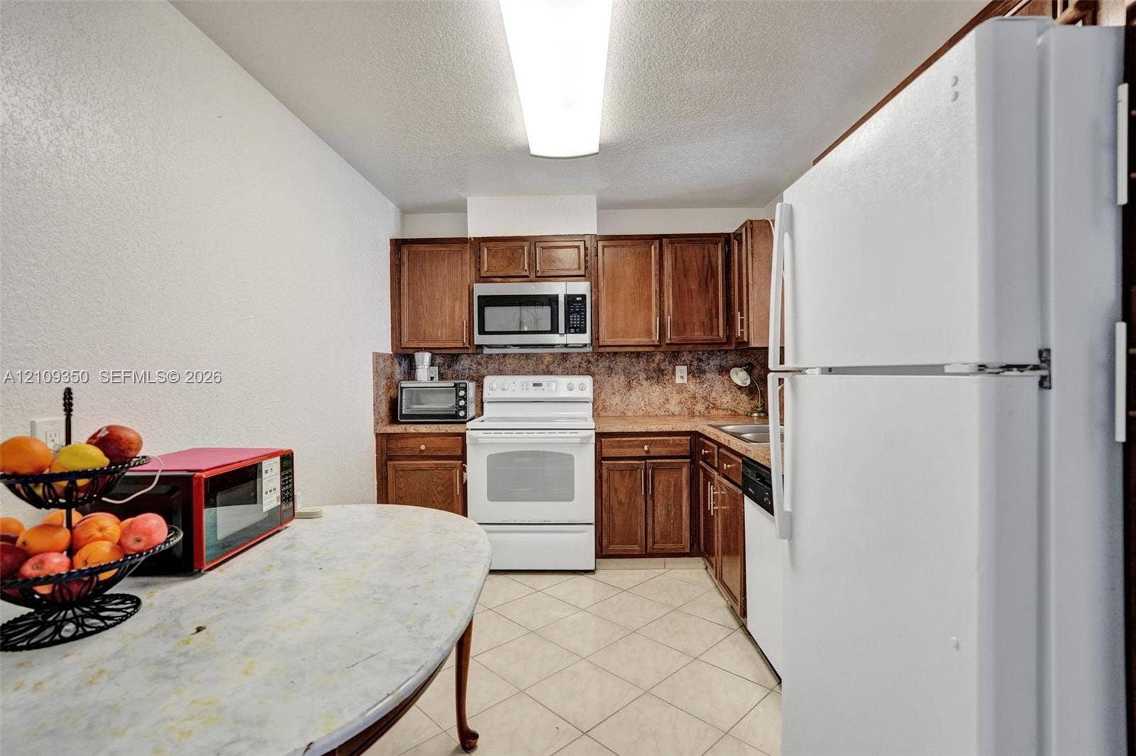 10777 W Sample Road, #616, Coral Springs, FL 33065 Kitchen featuring wood cabinetry, solid-surface countertops, tile flooring, and integrated white appliances including a range, microwave, and dishwasher