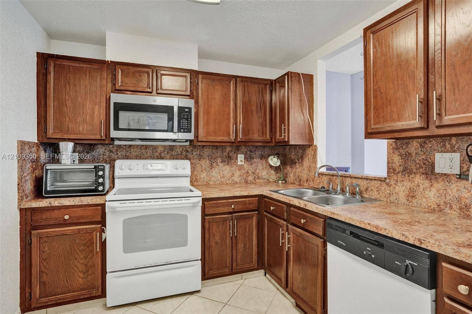10777 W Sample Road, #616, Coral Springs, FL 33065 Kitchen featuring wood cabinetry, stone-finish laminate countertops, dual-basin stainless steel sink, tile flooring, and integrated microwave