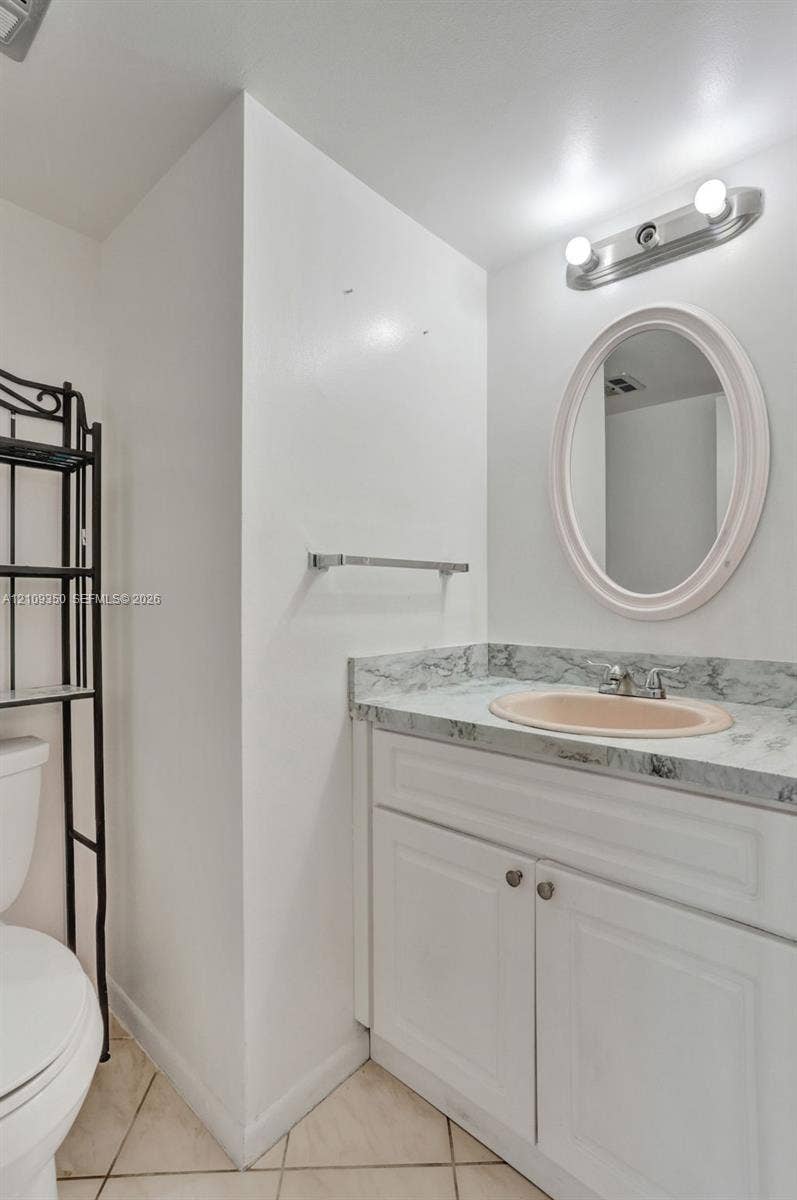10777 W Sample Road, #616, Coral Springs, FL 33065 Bathroom vanity featuring a stone-patterned countertop, integrated oval sink, white shaker-style cabinetry, and an oval wall-mounted mirror