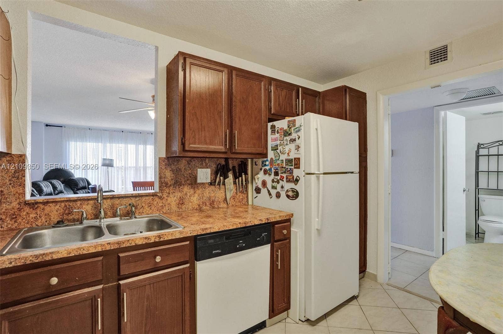 10777 W Sample Road, #616, Coral Springs, FL 33065 Kitchen featuring dark wood cabinetry, laminate countertops with a stone-finish pattern, a double-basin stainless steel sink, and a built-in dishwasher