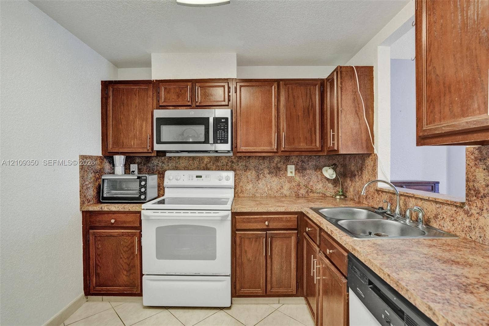 10777 W Sample Road, #616, Coral Springs, FL 33065 Kitchen featuring stained wood cabinetry, stone-finish countertops, tile flooring, and integrated stainless steel appliances including a range and microwave
